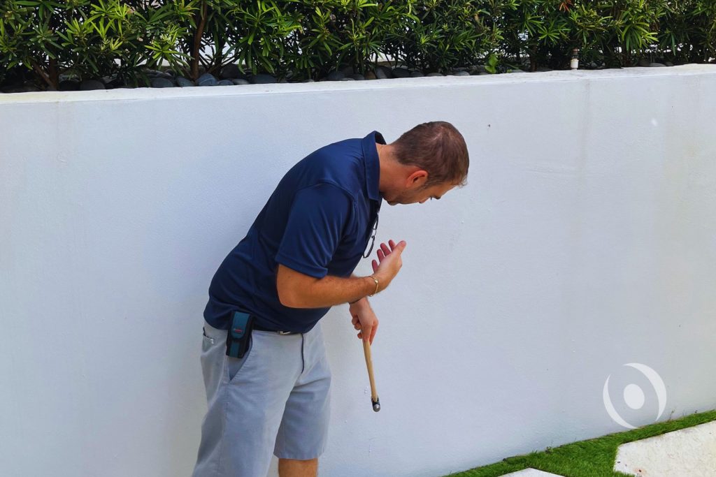 Structural inspector performing field assessment of residential wall using hammer test during site inspection