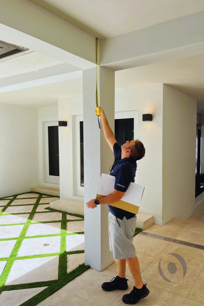 Structural inspector measuring column height and beam clearance in residential construction during on-site inspection