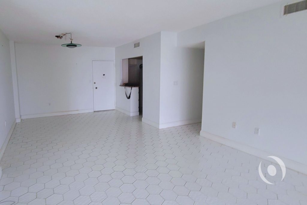 Original living room condition before architectural redesign showing outdated hexagonal tile floor and closed kitchen layout in Hallandale Beach condominium