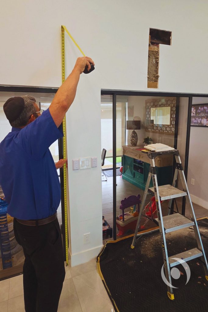 NOHMIS structural engineer conducting site inspection and measuring existing wall height during pre-design assessment for a residential addition in Boca Raton, Florida