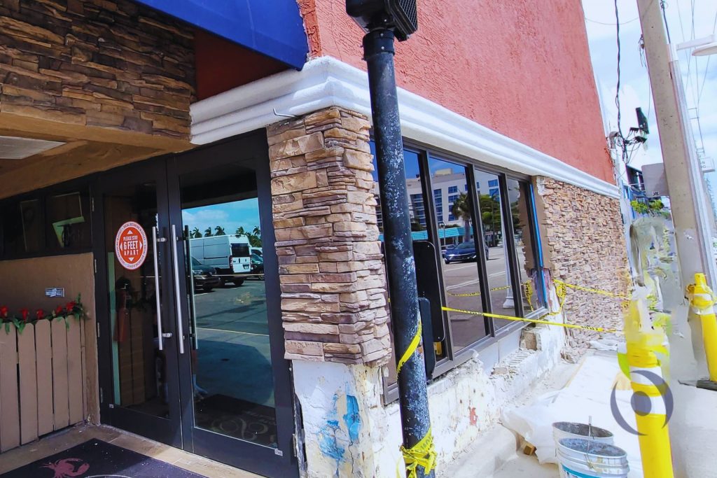 New stone facade installation in progress on restored structural column of commercial building in Broward County, Florida, with remaining concrete damage visible at lower section awaiting NOHMIS-designed repair per engineer of record construction documents
