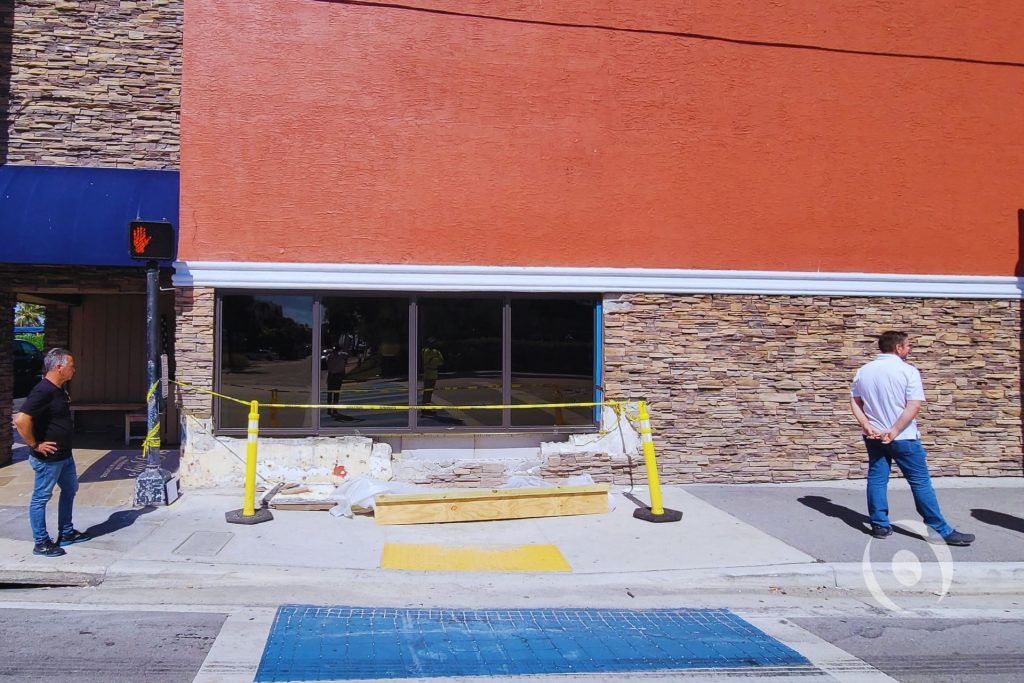 Street-level view of commercial building exterior on North Ocean Drive in Hollywood, Florida showing demolished CMU wall and safety barriers following vehicle impact, prior to NOHMIS structural engineering assessment and concrete restoration design