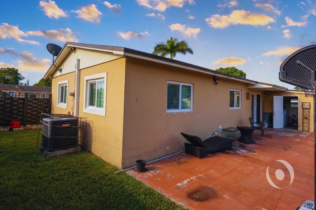 Rear exterior of completed single-family home addition in Miami-Dade County at golden hour showing full addition footprint, new windows, and patio area engineered by NOHMIS