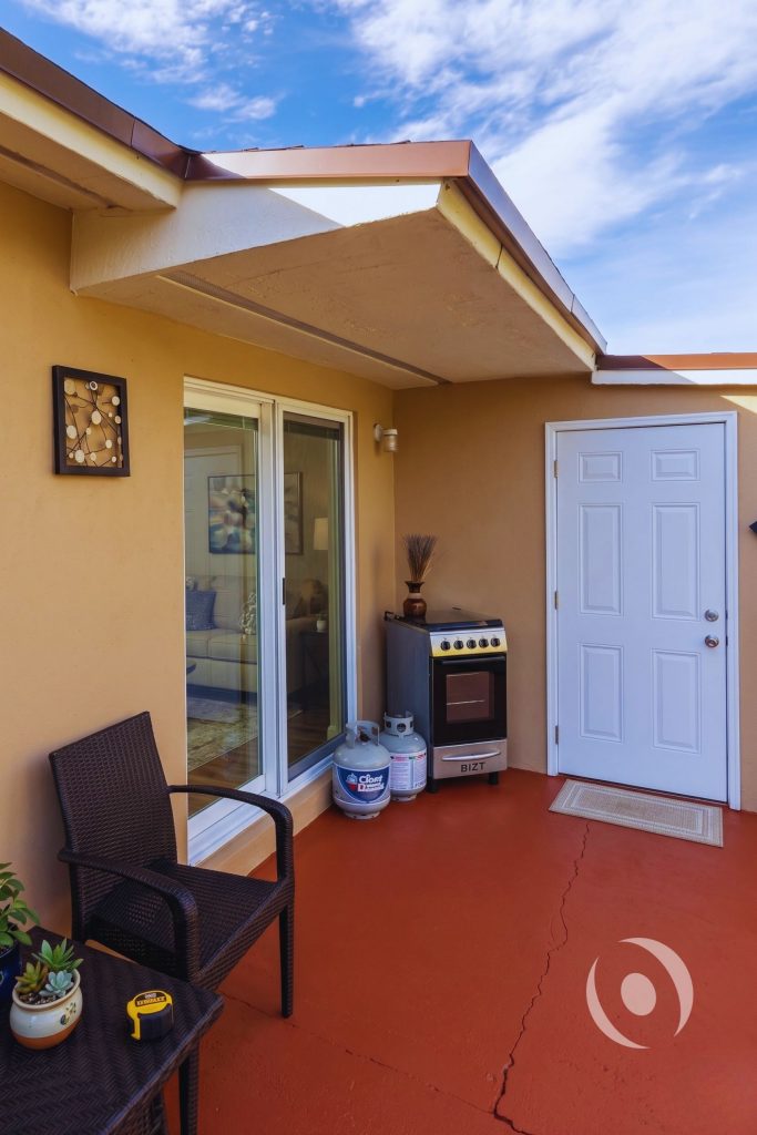 Architectural detail of completed home addition in South Florida showing covered patio, roof overhang soffit, sliding glass door, and exterior entry door designed by NOHMIS