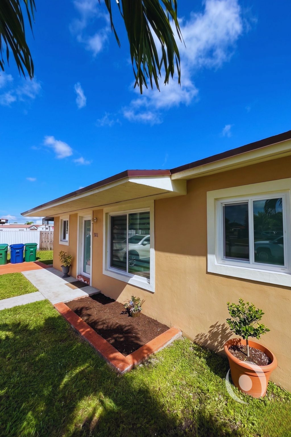 Front exterior of completed residential addition in Miami Gardens showing new impact windows, finished stucco facade, and landscaped entrance designed by NOHMIS South Florida