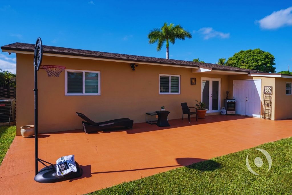 Wide rear exterior view of completed residential addition in Miami Gardens showing full stucco wall finish, new windows, outdoor patio, and lawn, engineered by NOHMIS South Florida