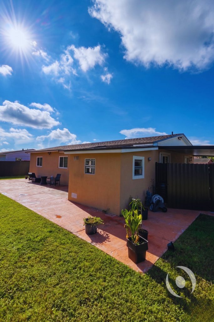 Side exterior view of completed single-family home addition in Miami-Dade County showing CMU construction, new roof framing, and finished stucco walls engineered by NOHMIS