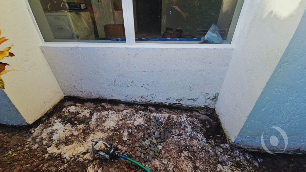 Foundation moisture damage and soil saturation along an exterior wall of a South Florida home with poor drainage conditions. 