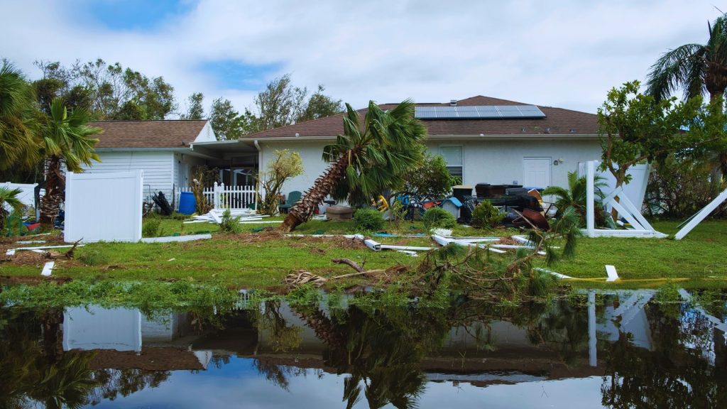 South Florida home with hurricane damage, broken fencing, fallen vegetation, debris, and standing water around the property.