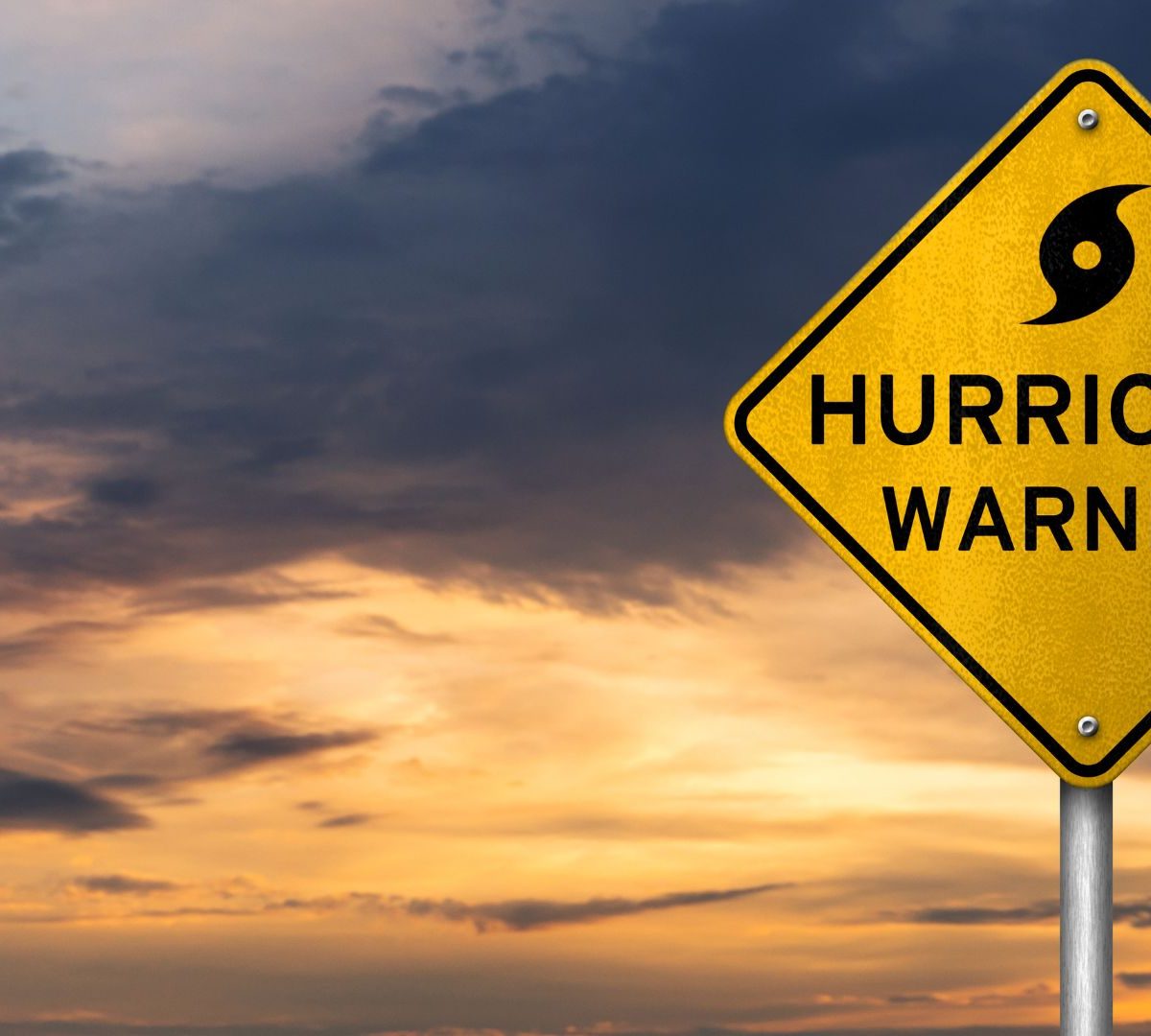 Hurricane warning sign under storm clouds representing hurricane season preparation in South Florida.