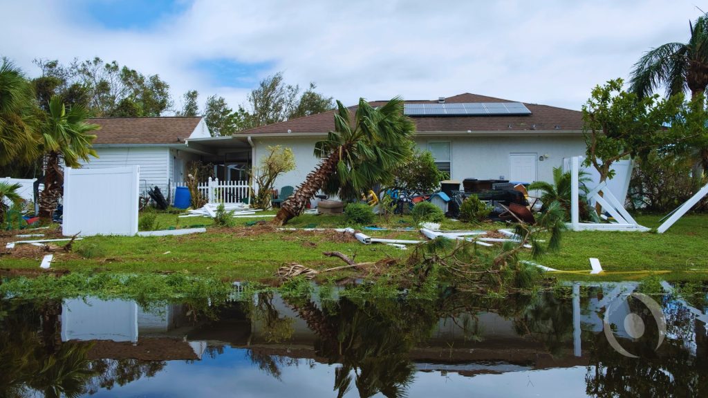 South Florida home with hurricane damage, broken fencing, fallen vegetation, debris, and standing water around the property.