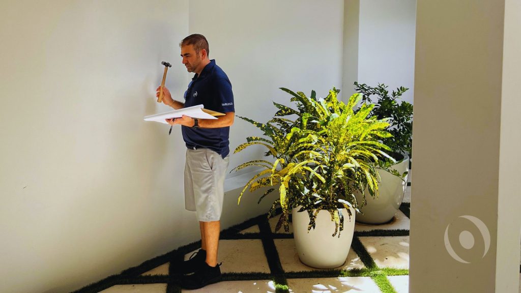 NOHMIS inspector examining an exterior wall with a hammer during a property inspection in South Florida.